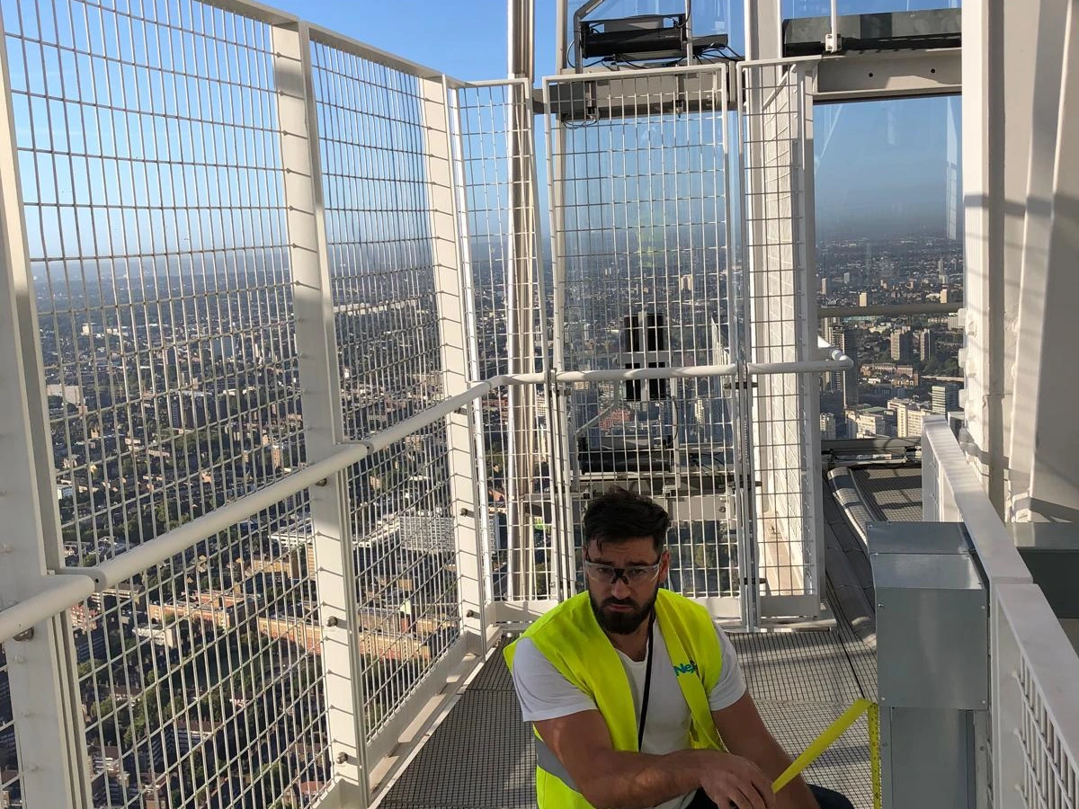 Electrician in hi-vis kneeling on a high-level steel platform fitting equipment