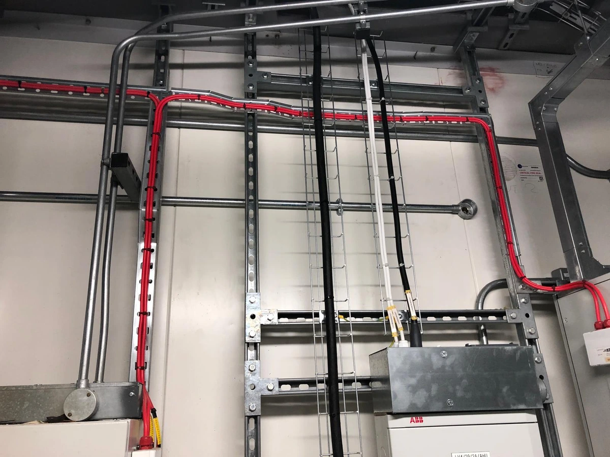 Steel conduit and red fire-rated cable fixed on strut above a distribution box
