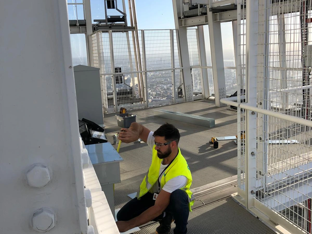 Electrician in hi-vis working on a high-level platform with city views behind