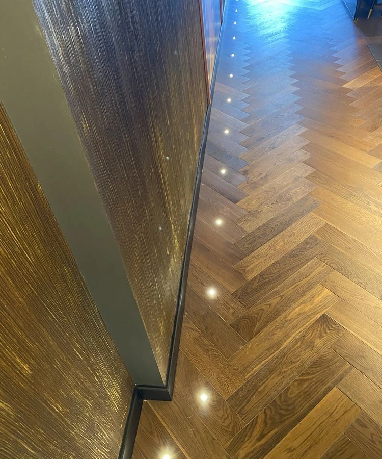 Recessed floor marker lights beside a wall panel on a herringbone timber floor